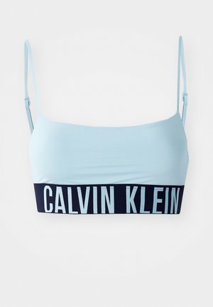 Hele sinine bralet õhukeste reguleeritavate rihmadega ja tumedast laevast sinisest bändist, millel on silmatorkavalt esitatud valge tekst "CALVIN KLEIN".