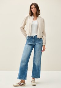 Ljusbeige bomberjacka, vit linne, högmidjade blå vida jeans och beige sneakers med vinröda detaljer. Enkla designelement.