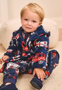 Accappatoio in pile blu navy con motivi di camion dei pompieri rossi e auto della polizia bianche, abbinato a pantaloni da pigiama coordinati. Texture morbida, design con cappuccio.