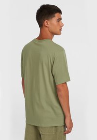 Camiseta de algodón color verde olivo con mangas cortas y cuello redondo, que presenta un ajuste relajado y costuras limpias. La textura parece suave y lisa.