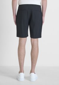 Shorts neri con vita elastica, due tasche posteriori e una texture liscia, abbinati a sneakers bianche su una superficie chiara.
