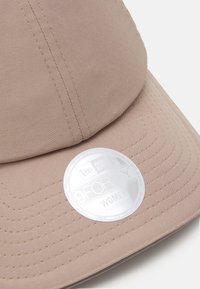 Casquette beige clair en tissu avec des coutures visibles. Elle dispose d'une couronne arrondie et d'un rabat courbé. L'étiquette métallique indique "New Era 9FORTY Women Adjustable."