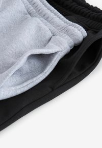Tres pares de pantalones cortos deportivos apilados: uno en gris claro y dos en negro. Hechos de una tela suave con cinturillas elásticas. Sin patrones ni detalles notables.