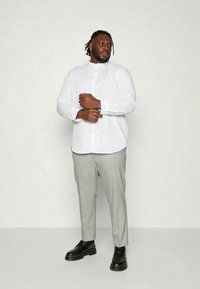 Camisa branca de mangas longas com colarinho mandarim, combinada com calças cinza claro com padrão xadrez e sapatos pretos. Tecido suave, corte ajustado.