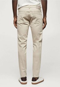 Jeans de mezclilla beige con corte slim, bolsillos traseros y una etiqueta tejida en la cinturilla, combinados con zapatillas blancas y marrones.