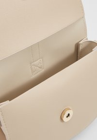 Beige faux läderväska med en slät textur, som har en guldknäppning och en ficka inuti, minimalistisk design och rena linjer.