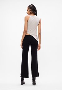 Top sem mangas cinza claro com um costado drapeado, combinado com calças pretas a abrir, oferecendo uma textura suave e uma silhueta moderna. Salto alto preto incluído.