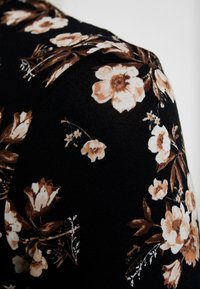 Svart tyg med stora blomstertryck i kräm och brunt, som har detaljerade blad och mindre blommor, något texturerad yta.