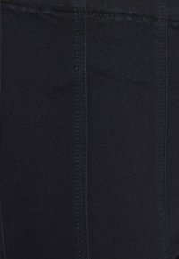 Tmavě modrá denimová látka s hladkým povrchem, viditelným šitím a jemnými modrými akcenty. Materiál je odolný a dobře přiléhá k tělu.