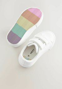 Baskets blanches avec une surface texturée, des sangles Velcro et une semelle en caoutchouc multicolore à motif en chevrons. L'intérieur présente une étiquette de marque.
