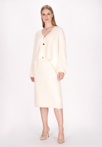 Crème ribbelde gebreide cardigan met een oversized pasvorm, knoopsluiting en een bijpassende rok tot de knie. Gladde textuur met een subtiele glans.