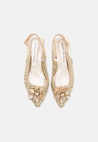 Zapatos slingback de tejido dorado con punta afilada, acentos metálicos y detalles florales adornados con perlas y cristales.