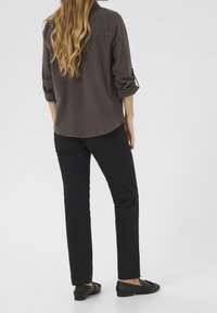 Chemise gris foncé à manches longues avec poignets retroussés, associée à un pantalon noir à jambes droites et des chaussures noires à enfiler, vue de dos.