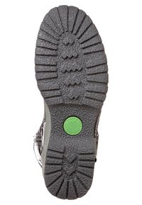 Suela de zapato de goma negra con un patrón de tracción pronunciado, que presenta un acento circular verde cerca del talón y una superficie texturizada para un mejor agarre.