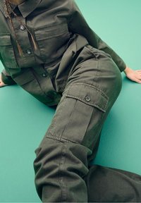 Olivew зеленый komplet cargo, składający się z koszuli z guzikami i dwoma kieszeniami na piersiach oraz pasujących spodni z bocznymi kieszeniami i teksturowanym wykończeniem.