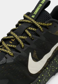 Μαύρο αθλητικό παπούτσι με υφή στο επάνω μέρος, πράσινες λεπτομέρειες και κίτρινα κορδόνια. Διαθέτει εμφανές λευκό λογότυπο Nike και σόλα με πράσινη γραφική υφή.