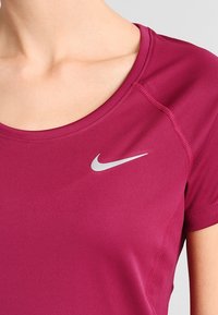 Camiseta deportiva magenta de manga corta, con un logo plateado de Nike en el pecho izquierdo y tela suave y elástica.
