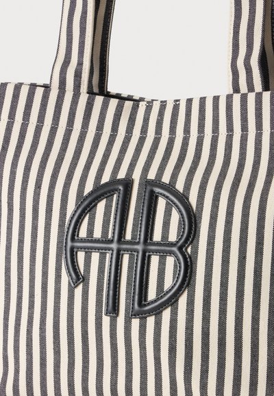 Gros plan d'un sac en tissu à rayures verticales noires et blanches avec deux poignées et un patch en cuir noir cousu avec un logo.