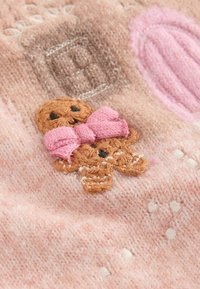 Rosa gestrickter Stoff mit einem gestickten Lebkuchenmann, der eine rosa Schleife trägt, akzentuiert mit weißen Punkten und einem strukturierten Hintergrund.
