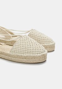 Espadrilles tissées beiges avec un dessus texturé, une pointe arrondie et une semelle en jute naturel tressé. Comprend des liens ajustables à la cheville.