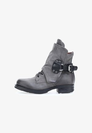 Sivi kožni gležnjača s preklopnim rubom, trakama s kopčanjem i vezanjem sprijeda. Ima zaobljen vrh i teksturiranu završnu obradu.