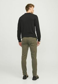 Camisa polo negra de manga larga con cuello, combinada con pantalones chinos verdes oliva. El conjunto presenta puños ajustados y bolsillos traseros. Zapatos negros.