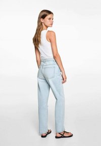 Jeans in denim chiaro con vita alta e vestibilità dritta, dotati di tasche posteriori e leggere sfumature. Indossati con una canotta bianca e sandali.