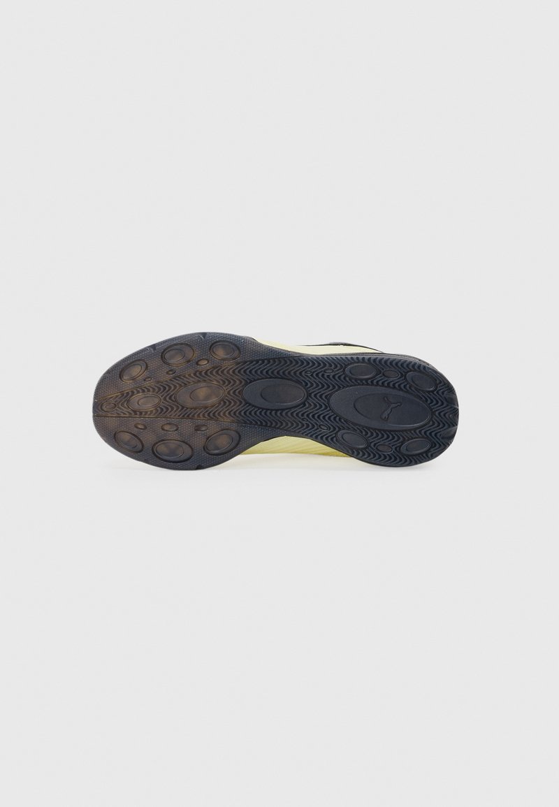 Semelle de chaussure de sport noire avec un intercalaire en caoutchouc jaune texturé et des motifs de grip circulaires. Présente une finition lisse et des couleurs contrastées.