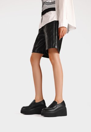 Scarpe piattaforma nere con finitura in pelle liscia e design slip-on, dotate di una suola spessa e prominente e uno stile minimalista.