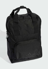 Mochila de tela negra con dos asas superiores, correas de hombro ajustables, bolsillo frontal con cremallera y superficie texturizada sutil. Presenta el logo de Adidas.