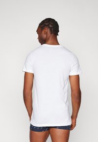 T-shirt en coton blanc à manches courtes, col rond et texture lisse, porté par une personne de dos.