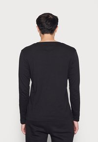 Mustassa pitkähihaisessa t-paidassa on pyöreä pääntie, normaali istuvuus, pehmeä puuvillakangas ja yksinkertainen kuosi, näkymä takaa.