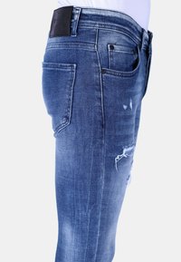 Blauwe denim jeans met een slim fit, versleten details met rafelige randen en een zwarte leren label op de tailleband.