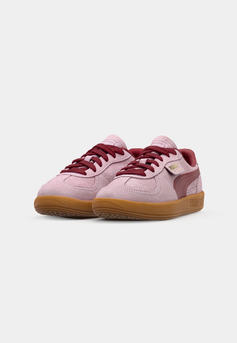 Des baskets en suède rose avec des accents bordeaux, un design à lacets et une semelle en caoutchouc. Le logo PUMA est affiché sur le côté en or. Silhouette basse.