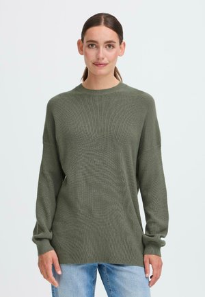 Oliven grønn oversized genser laget av teksturert strikket stoff, med lange ermer og rund hals, kombinert med lyseblå jeans.