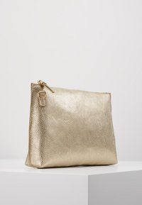 Metalická zlatá kabelka na ruku s texturovaným povrchem, s uzávěrem na zip a malým detailem očka na boku. Obdélníkový tvar s plochým dnem.
