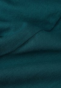 Tessuto turchese, con una trama testurizzata a linee diagonali, drappeggiato e sovrapposto, che mostra una superficie liscia e morbida.