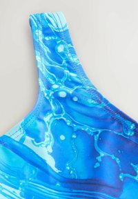 Kék fürdőruha pánt vízhullám mintával és részletes varrással világos háttéren.