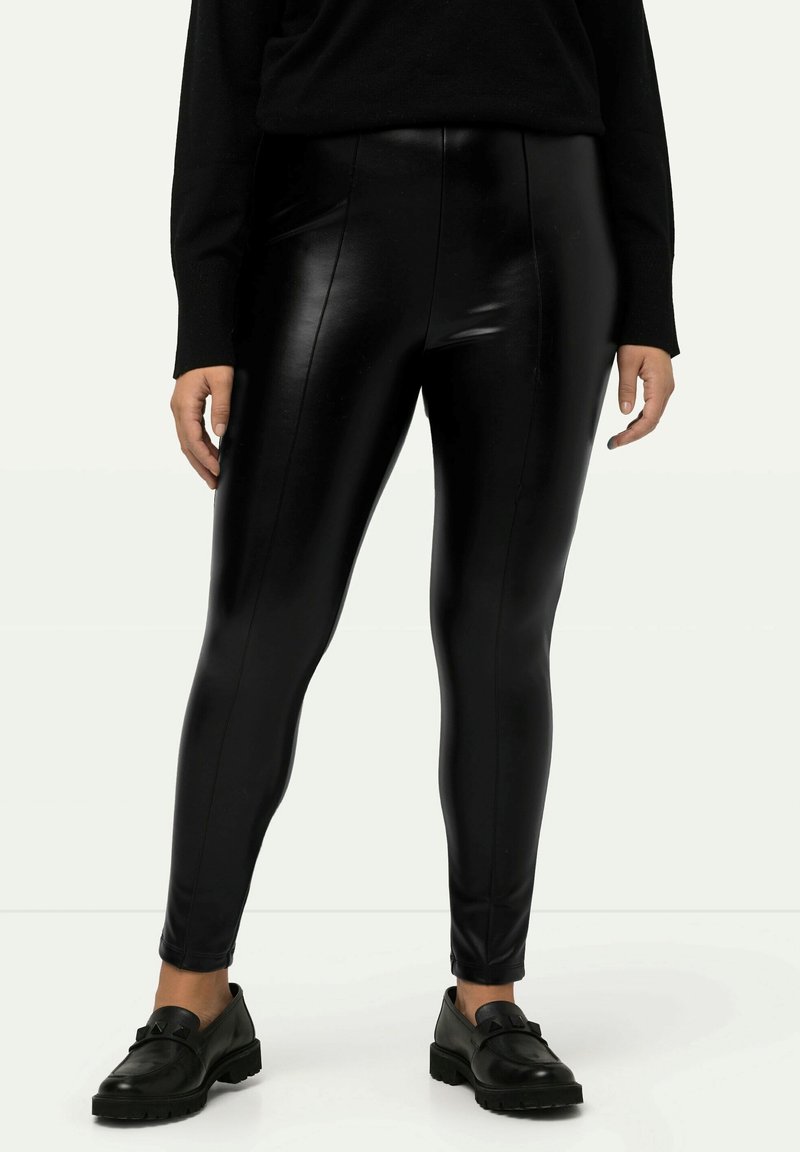 Leggings en cuir synthétique noirs avec taille haute, texture lisse et coutures latérales cousues. Associés à des mocassins noirs pour un contraste.