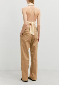 Tan wijde leg broeken met een gladde textuur, voorzien van zijzakken en een achterpand, gecombineerd met een lichtbeige haltertop met een strikje.