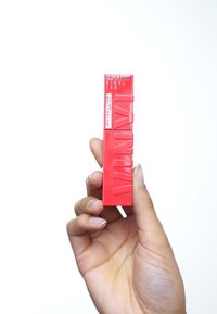 Röd läppstiftsrör med en matt, texturerad yta. Har djärva präglade bokstäver, rektangulär form och standard skruvkonstruktion.