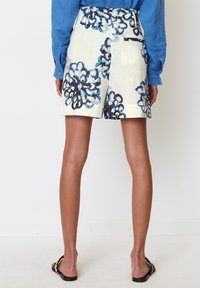 Shorts en lin blanc avec motif floral bleu, longueur mi-cuisses, et poches arrière. Associés à une chemise bleue à manches longues.