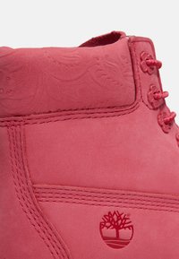 Stivale in suede rosa con motivo floreale embossato, cuciture a contrasto e sei asole decorative per i lacci con un logo ad albero sul lato.