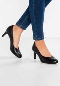 Czarne skórzane szpilki o gładkim wykończeniu, okrągłym nosku i smukłej sylwetce, zestawione z ciemnoniebieskimi dżinsami sięgającymi kostek.
