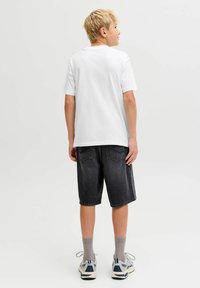 Camiseta blanca de algodón, pantalones cortos de mezclilla negra, calcetines grises y zapatillas. Costuras visibles en los pantalones cortos y un diseño limpio.