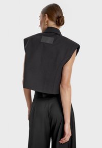 Czarny krótki bezrękawnik z wydłużonym kołnierzykiem, z prostokątną skórzaną łatką z tyłu i gładką teksturą materiału.