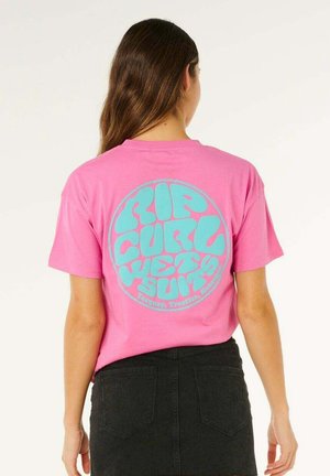 Kobieta z długimi brązowymi włosami, ubrana w różowy t-shirt Rip Curl z niebieskim napisem oraz czarną jeansową spódnicę, stojąca tyłem.