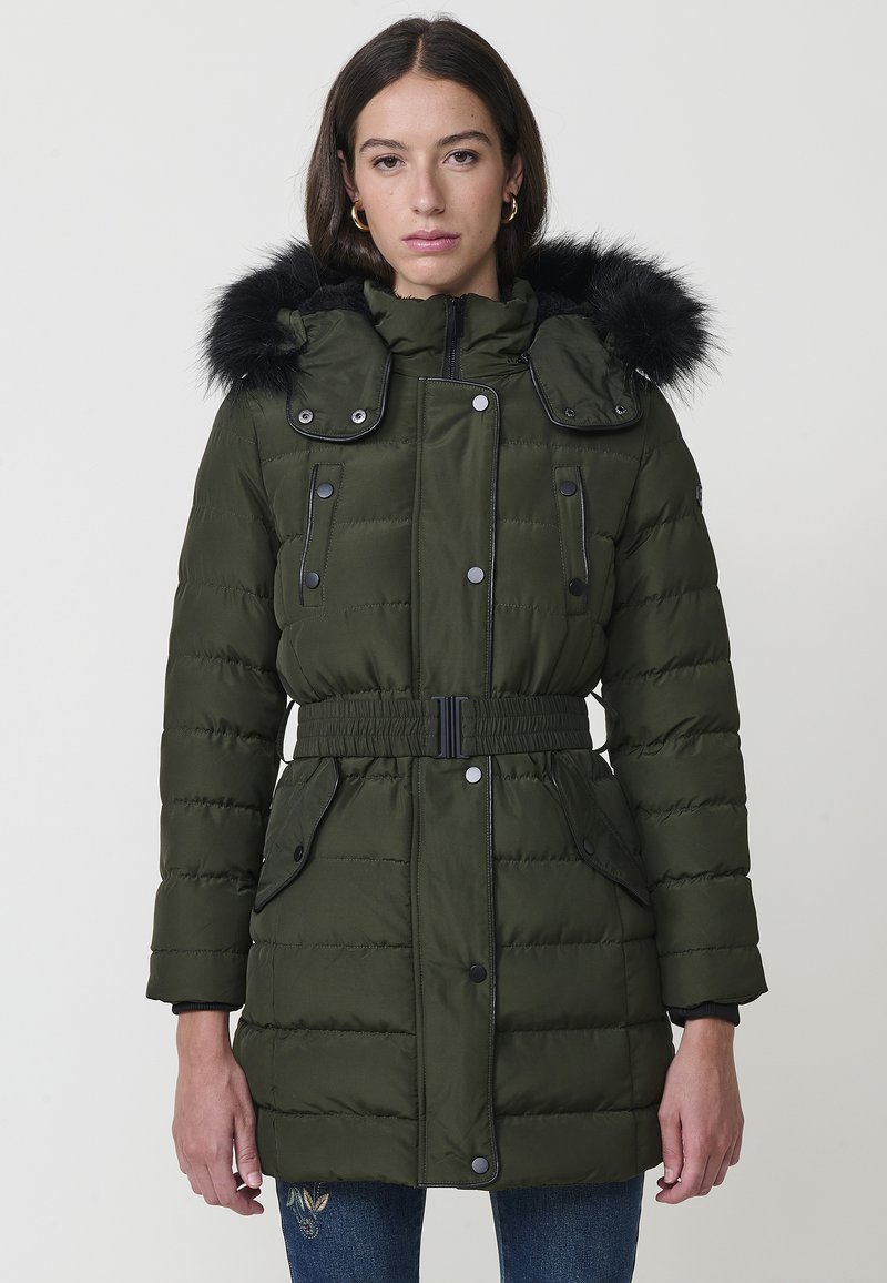 Chaqueta de plumas acolchada verde con capucha forrada de piel, acentos negros, cintura ceñida con cinturón y bolsillos abotonados. Textura suave y diseño estructurado.