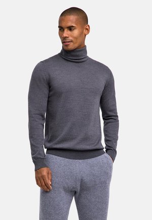 Golf z kołnierzem w ciemnoszarej wełnie, z długimi rękawami i prążkowanym wykończeniem. W połączeniu z jasnoszarymi, teksturowanymi spodniami.