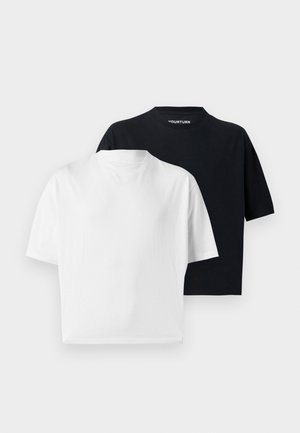 Dwie modelki ubrane w czarne, oversize'owe t-shirty, szerokie spodenki w prążki, białe skarpetki, czarne buty i ciemne okulary przeciwsłoneczne na białym tle.